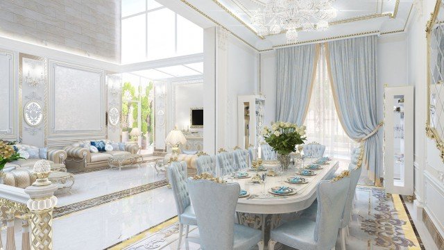 This picture shows a luxurious interior design with a white and gold theme. The room features two white sofas with gold accents, an ornate coffee table, a luxurious chandelier, and large white curtains that hang from the ceiling. The walls are painted white and feature decorative artwork. The floor is covered in a white and gold patterned rug.