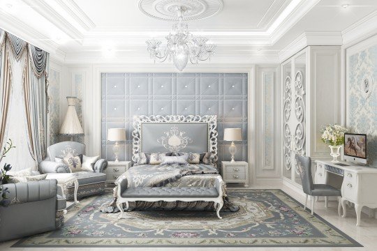 The picture shows a modern interior design for a bedroom. It features a luxurious bed with a light grey headboard and white bedding, as well as a dark grey accent wall and seating area. The room also includes a white side table, a beige decorative rug, and a light grey and white patterned wallpaper. A pair of large windows with black curtains lets in plenty of natural light, completing the look.