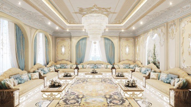 The picture shows an elegant, modern living room design. It features an off-white couch and matching armchairs arranged around a round glass coffee table with an ornate metal base. The pristine white walls are offset by lush curtains in shades of beige and gold. A crystal chandelier hangs over the seating area, while golden accents can be found throughout the room, including a gilded fireplace accent and sconces. An ornate clock is situated on the mantle, and a bright abstract painting adds a touch of color to the space.