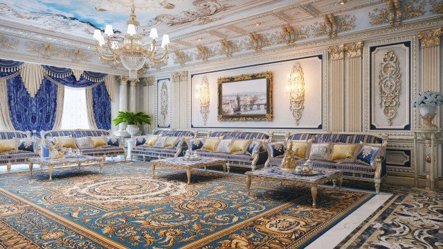 This picture is a rendering of an upscale luxury living space. It features a modern living room with an open floor plan, including beautiful marble and travertine floors, grand columns, a large flat screen television mounted on the wall and two modern capitonné gray sofas facing each other. The sofas are accented by several elegant end and coffee tables in various shapes and sizes, along with several pieces of art decorating the walls and shelf spaces. The overall effect of the room is vibrant, luxurious, and capable of hosting friends and family with comfort and grace.
