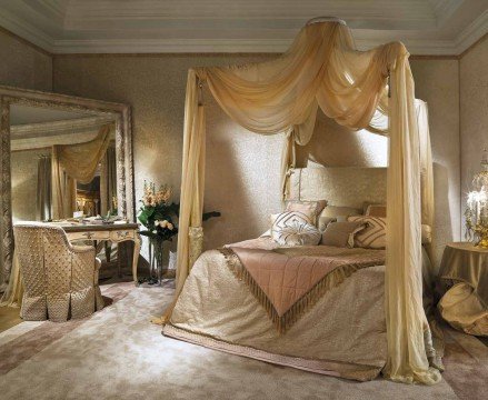 A luxurious bedroom with cream coloured walls and an immense bed area, decorated with intricate wood work and a chandelier above.