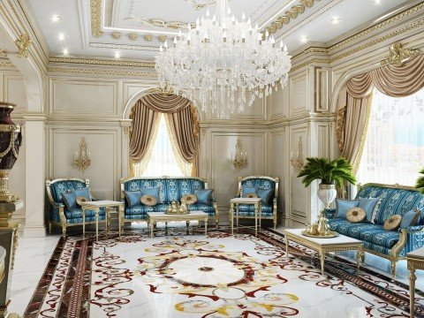 This picture shows a luxurious, modern sitting area featuring beige leather sofas and armchairs with ornate arm details. The furniture is situated around a central, low-level coffee table which is adorned with a metallic tray and a vase of flowers. The walls and floor are decorated with a rich textured wallpaper and an all-over patterned carpet respectively, and an elegant chandelier hangs from the ceiling.