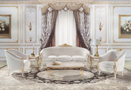 This picture shows an elegantly designed interior space within a home. The walls are covered in a light beige wallpaper with an intricate flower pattern, and the floor is covered in cream-colored parquet tiles. A gold-framed mirror hangs on the wall above a wooden sideboard holding a few ornaments, and a white and gold armchair is placed in the corner with a cushioned seat for comfort. Large windows flood the room with natural light, and a crystal chandelier hangs from the ceiling to further illuminate the space.