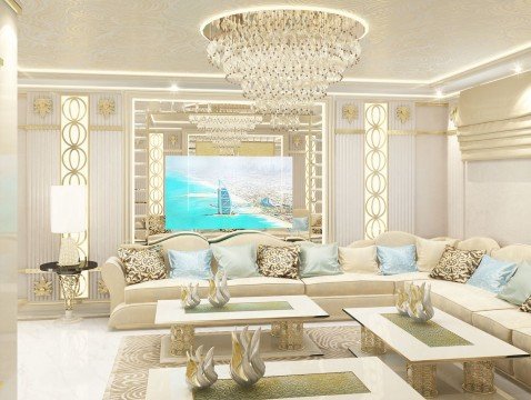 This picture shows a luxurious living room with a grand chandelier hung from the center of the ceiling. The walls are covered in a neutral wallpaper and adorned with gold, diamond-patterned panels. A white marble fireplace is featured in the corner, and two blue velvet sofas are placed on either side. The floor is covered in a rich navy rug and a few gold accents can be seen around the space.