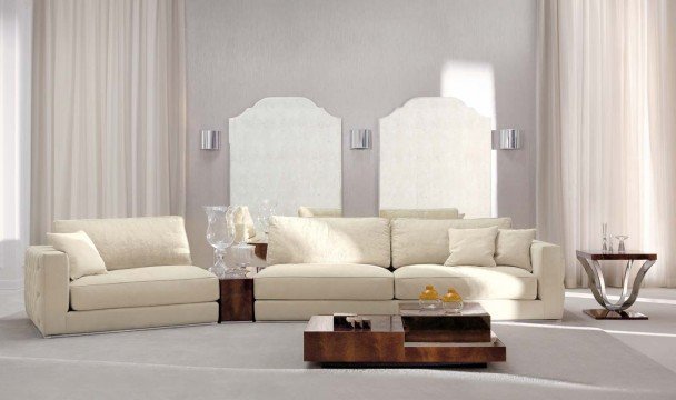 This picture shows a luxurious interior design of a living room. The furniture is covered in champagne velvet upholstery which adds a touch of glamour and elegance to the room. The walls are painted a pale yellow color and feature a series of framed artwork. The centrepiece of the room is a stylish crystal chandelier hanging from the ceiling, adding a sparkle to the otherwise muted tones. The floor is also covered in a cream and light brown patterned rug that ties in nicely with the surrounding decor.