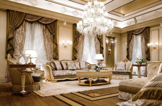 This picture shows an elegant, luxurious living area with white and gold furniture and decor. The neutral colors of the walls and furniture are complemented by gold accents such as a gold-framed mirror, lamp and table. There is a comfortable sofa in the center of the room upholstered in a muted beige fabric with ornate gold pillows. The room is well-lit with a large crystal chandelier and other decorative lighting fixtures. The design is timeless and classic, creating an inviting atmosphere.