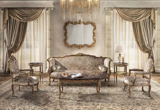 This picture is showing a luxurious and elegant bedroom designed by the interior design firm Antonovich Design. The room features a stunning crystal chandelier, dark wood furniture, and plush cream colored rugs and upholstery. The walls are covered with a pale gold damask wallpaper, and the floor is made of white marble. Gold accents are used throughout the room to give it an opulent and regal feel.