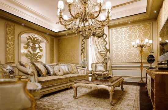 This picture shows a luxurious interior design with a curved staircase in the middle of the room. The staircase has ornate wood railing and carved balusters made from a light-colored wood. The walls and floor are covered in marble and have intricate detailing. On either side of the staircase there are two tall, gold-framed mirrors, and the whole room has luxurious golden accents.
