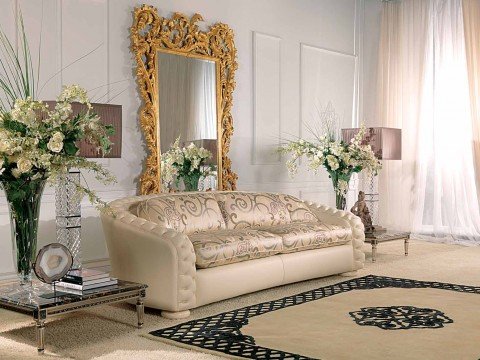 This picture shows a modern bedroom design with a luxurious black and gold theme. There is a large bed with a black and gold headboard, which is flanked by two mirrored bedside tables. The walls are painted black and there is an ornate gold chandelier hanging from the ceiling. In front of the bed is a velvet tufted bench and there is a small desk with an upholstered golden chair in the corner. On the walls there are several abstract art pieces and a large patterned rug completes the look.