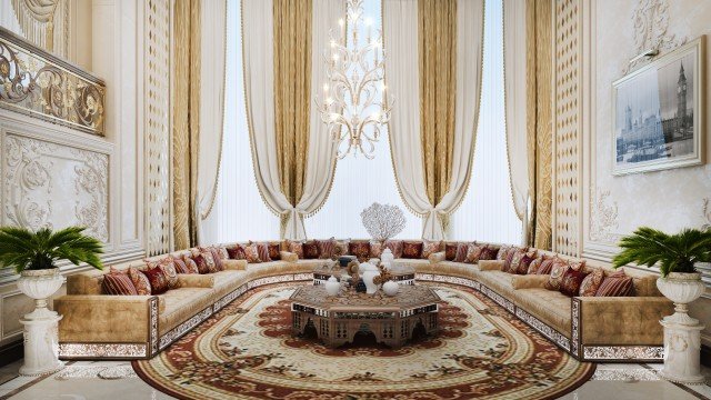 This picture shows a modern, luxurious living room. The walls are painted in a pale gray color, and the ceiling has recessed lighting. There is a white marble floor with a rug in the center of the room. On one side of the room, there is a large piece of wall art over a beige sofa. The other side features an armchair and two smaller sofas arranged around a coffee table with a vase of fresh flowers. In the middle of the room, there is a fireplace with glass doors and a black mantle with two candle holders and two small sculptures.