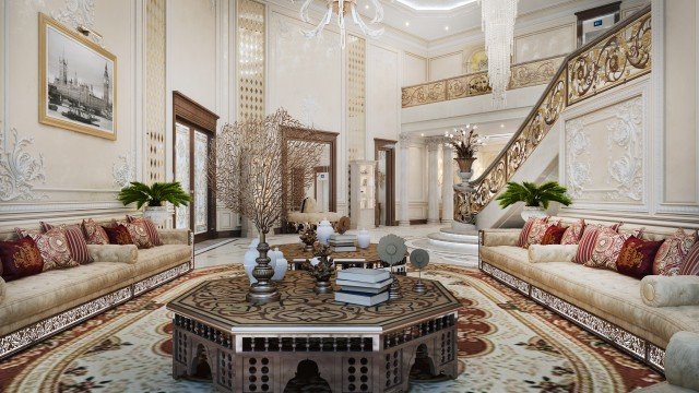This picture shows luxury interior design with a large staircase. It features a grand, marble staircase with gold accents on the railing. The walls are painted in a warm beige color and have white detailed moldings to accentuate the height of the space. There is also a large, round chandelier hanging from the ceiling. The floor is finished with parquet wood panels in a light color.