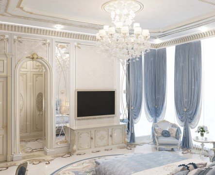 This picture shows an opulent bedroom interior in shades of white and silver. It features a luxurious four-poster bed with ornate columns and headboard, draped in sheer white fabric with silver accents. On the white walls hang two large picture frames. A plush, white sofa sits against one wall near a built-in set of shelves. A crystal chandelier hangs overhead, adding an elegant touch to the room.