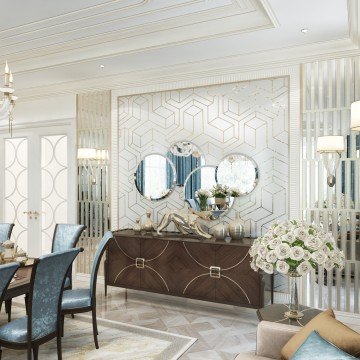 This picture shows a luxurious living room with a light marble floor and patterned wall panels. The walls are adorned with white and gold crown molding, and the furniture is upholstered in a creamy beige fabric. A large golden mirror hangs above an attractive mantelpiece, and a white velvet sofa is paired with a glass-top coffee table and two white armchairs. An elegant brass chandelier is suspended from the ceiling and adds an extra touch of glamour to the decor.