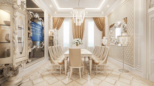 This picture shows a traditional and elegant dining area. The room features intricate detailing, including a dark wood paneled wall, white crown molding, and luxurious light fixtures. In the center of the room is a rectangular table with four light-colored chairs. At the far end of the room is an ornate buffet in matching light tones that provides storage for china and décor. A large window allows for plenty of light to come through, illuminating the warm interior.