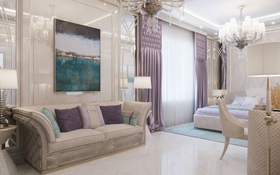 The picture is of a luxurious, modern living room. It features a beige L-shaped couch, several bright accent pillows, a large floor-to-ceiling window with sheer curtains, and a long, off-white area rug. There is also a modern glass coffee table and a large television mounted on the wall. The walls are decorated with mirrors and artwork, and a small plant can be seen on the shelf.