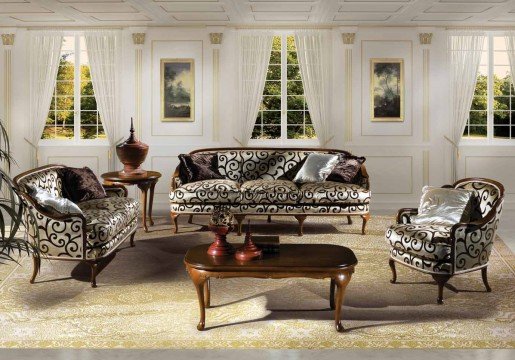 This is a picture of a luxurious, modern living room. It features a white, grey, and gold color palette. The walls and ceiling are white with gold accents, while the furniture is light grey with gold detailing. The room contains a large sectional sofa, two armchairs, a glass coffee table, a rectangular center table, a patterned rug, a black fireplace, and artwork on the wall. The space exudes elegance and sophistication.