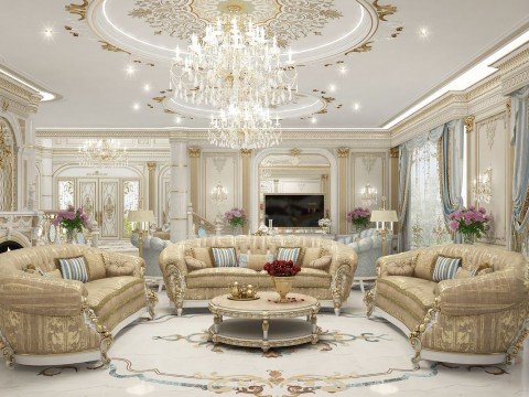 This picture shows a large formal living room with a black and white theme. A grand chandelier hangs from the ceiling, and there are several luxurious armchairs and sofas in a variety of styles arranged around the room. There is a decorative fireplace, and two white walls with large black and white portraits hung on them. On either side of the fireplace there are tall white columns and various pieces of furniture, while plants and sculptures provide additional decoration.
