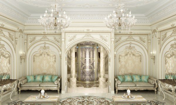 This is a picture of an elegant luxury living room with a classic beige and gold color palette. The room features a white marble fireplace with a beige stone facing, a set of chandeliers hanging from the white tray ceiling, and two comfortable tan sofas separated by a glass-top cocktail table. The walls are painted a light beige, with striped wallpaper and patterned rugs adding texture to the space. On the left side of the room, a golden armchair sits in front of a floor-to-ceiling window that overlooks a pool outside.