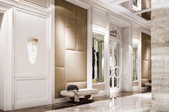 This picture appears to be an interior design of a luxurious living area. The room features a white sofa with a patterned gray and cream throw, an ornate chandelier with crystals suspended from the ceiling, a wall of floor-to-ceiling windows, and a large silver armoire along the back wall. Additionally, there are various accent pieces such as a gilded mirror, a large painting on the wall, and a geometric rug.