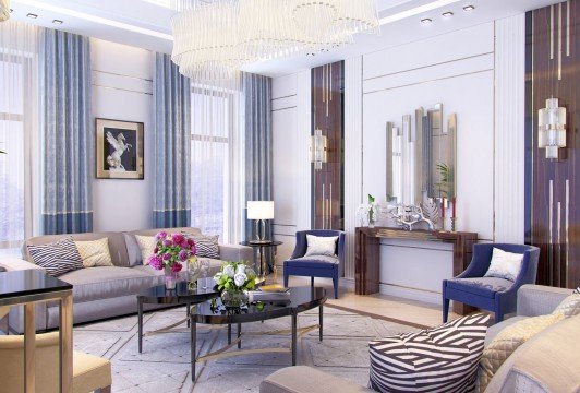 This picture shows a luxurious contemporary living room with a blue velvet tufted sofa, purple and gold accent cushions, a glass coffee table, and a white and gold chandelier. The walls feature gray tones, white crown molding, and a large painting in stone tones. There is also a white brick fireplace with a white marble mantelpiece and gold accents.