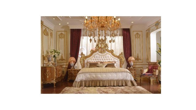 This picture shows an opulent living room designed by Antonovich Design. The room features a large white sectional sofa with multiple plump pillows, an ornate crystal chandelier hanging from the ceiling, and a heavy, luxurious gold-trimmed velvet curtain framing the windows. The walls have a warm ivory wallpaper with intricate patterns and a glossy marble floor adds to the sophisticated atmosphere.