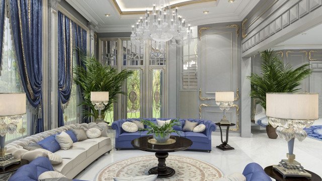 This picture shows a luxurious modern living room with a contemporary interior design. The room features a sectional sofa situated beneath a large window, illuminated by recessed lighting. There are several stylish end tables and armchairs scattered around the room, as well as a large area rug in the center. The walls are decorated with abstract art and there is an eye-catching chandelier hanging from the ceiling.
