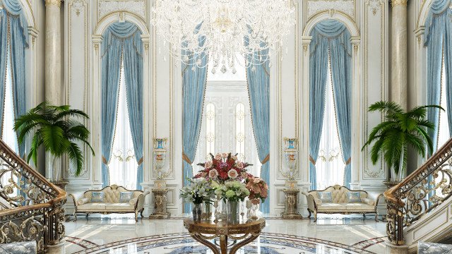 The picture shows a large, grandiose living room with a grand ceiling and ornate chandelier. The furniture is luxurious and comfortable while the walls are decorated with exquisite patterns. There are two double doors in the background leading out to a balcony and the overall design creates a warm and cozy environment suitable for relaxation and entertaining.