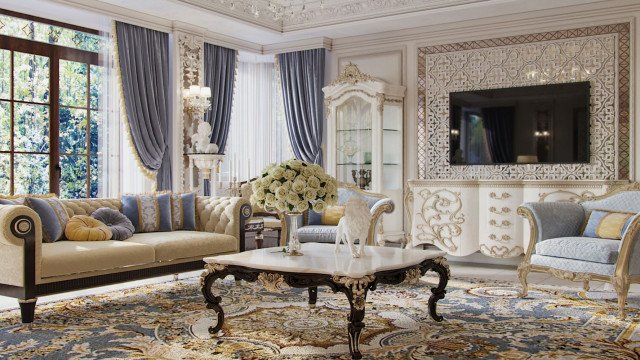 This picture shows a modern, luxurious bedroom designed with gold-trimmed furniture and accessories. The walls are painted in a light beige colour and the floor is covered with an ornate rug. The bed frame is upholstered with a velvet tufted headboard and a white bedspread. A pair of chairs sits at the end of the bed and is surrounded by a glass and metal chandelier, candelabra table lamps, and mirrored nightstands. The room is accessorized with a few decorative objects like a golden vase and a gold framed