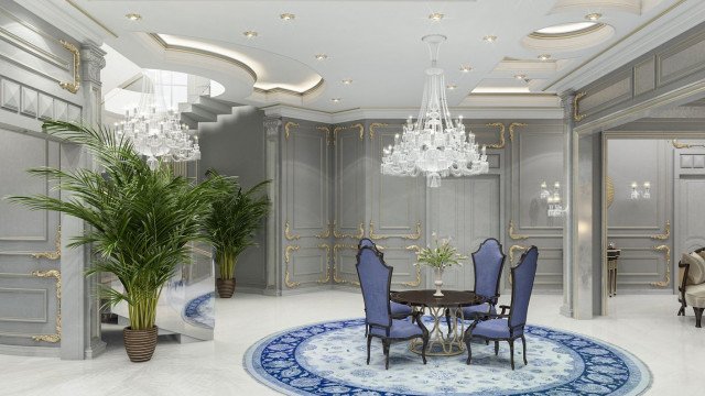 This picture shows a luxurious and elegant living room. The room has a high vaulted ceiling with a stunning crystal chandelier hanging from it. The walls are decorated with intricate moldings and a large mirror which is framed in luxurious gold leaf. The furniture is upholstered in a gorgeous white and gold fabric, while the floor features a beautiful rug with a mix of neutral colors. The overall look of the room is extremely opulent and grand.