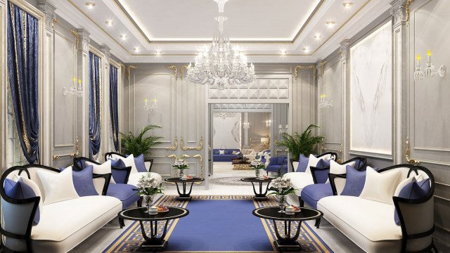 This picture shows a luxurious living room designed by interior design firm Antonovich Design. The room features an off-white sofa and armchairs, with several decorative pillows and a plush rug in the center of the seating area. The walls are painted in a light shade of gray and adorned with large abstract art pieces and gilded mirrors. The room also includes a marble fireplace and modern lighting fixtures.