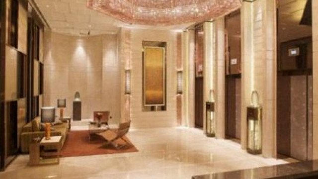 This picture shows an elegantly designed bathroom, featuring a large shower with glass walls, a free-standing marble bathtub, and a double vanity. The room is decorated with a luxurious rug, a chandelier, and two beautiful wall sconces. The walls feature natural stone tiles, and the floor is laid in marble.
