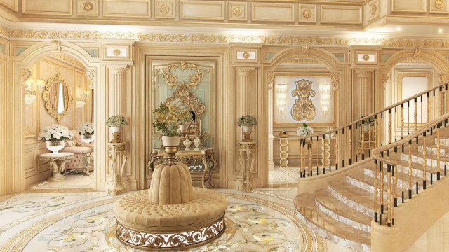This picture shows an interior design created by Antonovich Design. The room has a modern, luxurious feel with mirrored walls, ornate ceiling details, intricate crown molding, and an illuminated crystal chandelier. The floor is marble with gold inlay, and there is a large, decorative area rug in the center of the room. A brown leather sofa and two armchairs are placed around a glass coffee table.