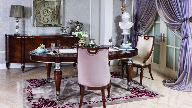 This picture shows a beautiful, grand living room filled with detailed and luxurious furnishings. The walls are adorned with a striking patterned wallpaper, while the floor is made of glassy marble tiles. Upholstered furniture in coordinating colours of beige and brown cover the space, while two modern vases add visual interest. Natural light fills the room, creating a warm and inviting atmosphere.