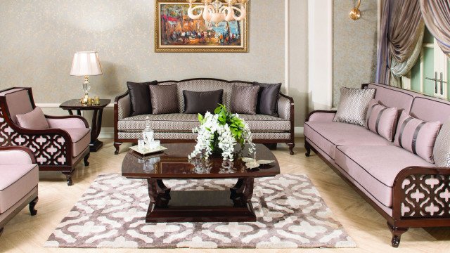 The picture shows a modern living space with a large abstract painting on the wall. There are various pieces of furniture such as a sofa, coffee table, armchair, and ottoman in the room. The colors used in the room are mostly neutral such as white, beige, and grey. The large abstract painting is the main focal point in the room and provides the room with a burst of color.