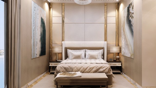 This picture shows a modern luxury bedroom interior. The room features a large four-poster bed with light beige drapery hung along the bed posts, a white and gold tufted headboard, and white and gray patterned sheets. The walls are painted in a light gray color and the floor is covered in a beige carpet. There are two white modern chairs sitting opposite the bed as well as a white and gold side table containing a golden lamp. The overall look of the room is contemporary and sophisticated.