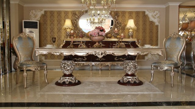 This picture shows a luxurious marble and stone floor in a grand entryway. The space features elegant golden accents, beige walls, large windows, and a chandelier hanging from the ceiling. The floor is composed of large black and white squares with gold lines along the perimeter, adding a touch of opulence to the room.