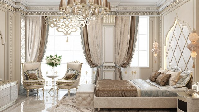 The picture shows an elegant bedroom interior design with a luxurious canopy bed in the center. The bed is covered in a white and silver velvet comforter and adorned with several white and silver pillows. The bed frame is decorated with intricate scrollwork, giving it a regal look. To the right of the bed is an emerald green upholstered armchair, while a simple grey nightstand sits to the left. On the walls are framed portraits and art prints, and the floors are covered in a light wood laminate. The room is illuminated by a few hanging pendant