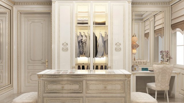 This is a picture of a modern luxury interior design by Antonovich Design. The room features plush white furniture with accents of gold and grey, carved wooden details, and a large crystal chandelier that dominates the central space. The walls are covered with white wainscoting and decorated with elaborate wall artwork, while the floor is covered in a marble tile pattern.