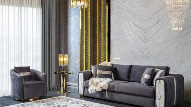 This picture shows a modern, luxurious living room designed by Antonovich Design. It features an elegant white and gold color palette, with hints of black and grey. The walls are painted in a glossy finish and adorned with gold accents, while the furniture pieces are upholstered in velvet fabric. Large windows bring plenty of natural light into the room, while the two crystal chandeliers provide warm ambient lighting. The overall design is finished with classic rugs, pillows, and decorative artwork.