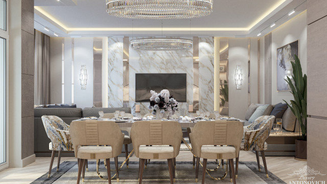 This picture is of a luxury dining room with a marble floor, a grand chandelier hanging from the ceiling, and a beautiful cream colored dining table that is surrounded by elegant chairs upholstered in white fabric. The walls of the room feature decorative molding with accents of gold and a wide mirror mounted above the dining table. There are also multiple ornate side tables and two stunning wall lamps that complete the look of this luxurious dining room.