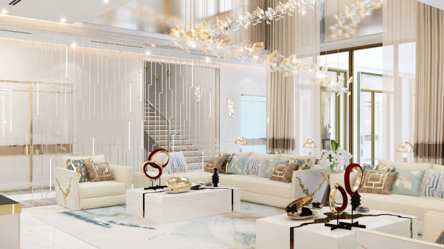 This is an artist's representation of a modern, luxury living room. The room features an off-white sofa with golden and beige accent pillows, a large window looking out onto an outdoor patio, a cozy armchair in a geometric pattern, an ornately carved coffee table, and a light grey area rug. On the walls hang several pieces of art, including an abstract painting and several framed photographs. A large potted plant sits in the corner near the window.