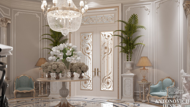 The picture shows a luxurious home interior with a large winding staircase, a grand chandelier and gold accents.