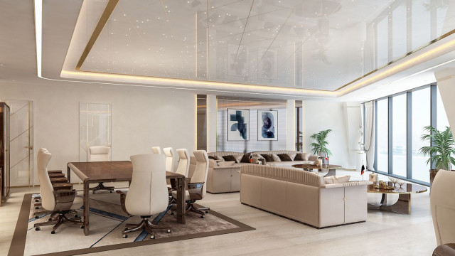 The picture showcases an elegant and luxurious living room with an emphasis on modern and contemporary design. The room is furnished with a comfortable, light grey couch and accent chairs with metallic touches, a large glass table, and a statement area rug in black and white. The walls are painted in a soft, warm beige hue and the windows are adorned with classic white draperies. The artwork on the walls exhibits a modern edge, completing the overall look.