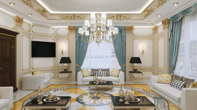 This picture shows a luxurious living room with a marble fireplace, wooden built-in cabinets, and a beige velvet sofa. The walls are painted in a neutral taupe color, and the floor is covered in light gray carpet. Modern art pieces adorn the walls along with intricate crown molding. A crystal chandelier hangs from the center of the room, adding a touch of glamour.