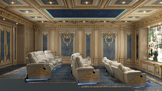 This picture is of an elegant and luxurious living room. The room features a light grey upholstered sofa and chairs, with accent cushions in navy and gold. A round side table sits between the sofa and one of the chairs. There is an ornately carved wooden coffee table in front of the sofa. On either side of the sofa are matching floor-to-ceiling windows with gold curtains. The walls are decorated with framed art, and a large crystal chandelier hangs from the ceiling.