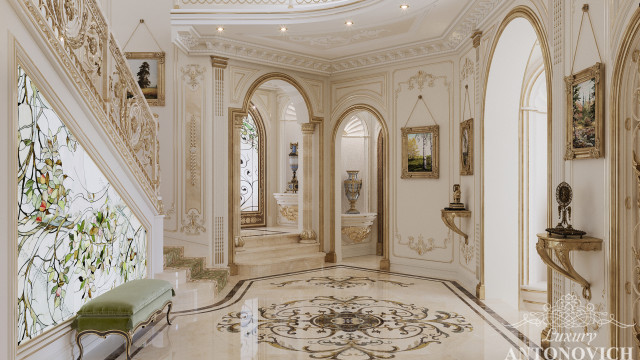 This picture shows a luxurious bathroom designed by Antonovich Design. The bathroom has a sunken tub with a marble ledge and gold faucets. The walls are adorned with intricate wallpaper and a textured tiles. Other features include marble flooring, a classic fireplace, and a built-in vanity with gold accents. The overall effect is one of timeless luxury.