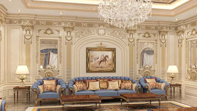 This picture shows a contemporary interior designed by Antonovich Design. It features a large living area with white furniture, a regal chandelier, and a grand marble fireplace. An elegant patterned rug rests beneath the furniture, adding a hint of color and texture to the space. The walls are adorned with a variety of artwork, adding a touch of artistry to the room.