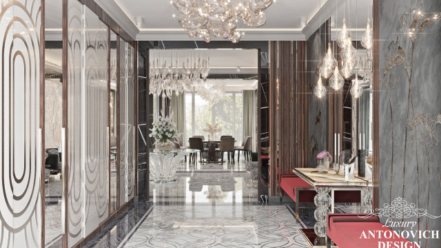 This picture shows a luxurious dining area with a built-in bench seating along one wall and a long, marble-top table in the center. The chairs and bench are upholstered in velvet fabric and the walls are accented with luxurious gold and silver detailing. A large crystal chandelier hangs from the ceiling and two modern mirrors hang on opposite ends of the room. There is also a luxurious marble fireplace on one side.