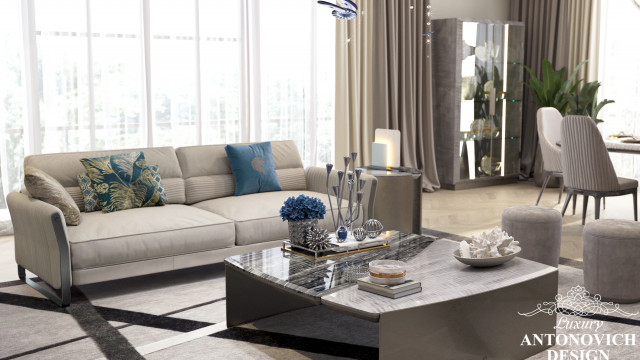 This picture shows a luxurious living room with a sleek, modern design. The room features an enormous window overlooking a stunning outdoor view, with plush white sofas and a large glass coffee table arranged in the center. The walls are painted a muted shade of beige, contrasted by the dark grey furniture and accessories. A glossy fireplace is featured prominently on one side of the room, adding a touch of warmth and sophistication.