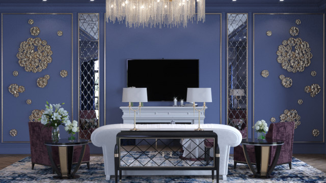 This picture shows a modern luxury living room interior design. It features a contemporary blue velvet couch with gold trim and matching gold accent pillows, an glass-top coffee table, and beige armchairs arranged around a patterned rug. The walls are painted an off-white color with a silver and gold decorative wallpaper, and the room is illuminated by a large chandelier and wall sconces.